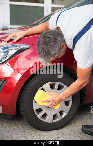 Reife männliche Heimwerker Reinigung Auto Rad mit Schwamm Stockfoto