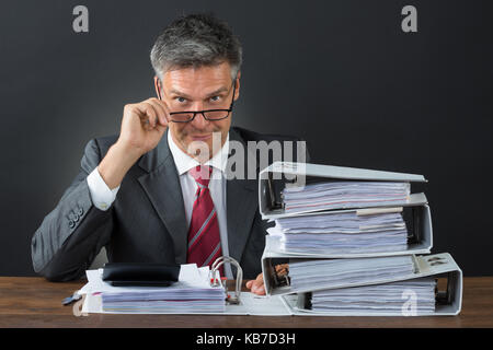 Portrait von zuversichtlich Geschäftsmann kontrolle Rechnung am Schreibtisch gegen grauer Hintergrund Stockfoto