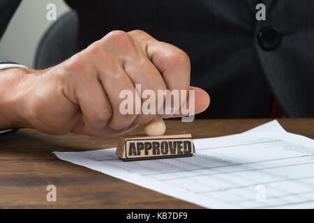 Zugeschnittenes Bild des Geschäftsmannes stanzen Dokument mit am Schreibtisch genehmigt markiert Stockfoto