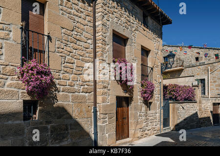 Schönes Steinhaus mit schönen vergitterten Balkon von wo aus Töpfen gehängt voller roter Blüten hängen. Elciego, Stadt von Álava, Baskenland, Spanien Stockfoto