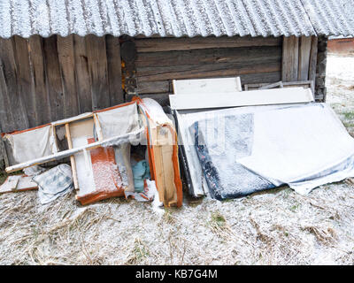 Alte kaputte Möbel mit Schnee in der Nähe einer verlassenen Holz- Haus oder Stall abgedeckt, Outdoor Winter geschossen Stockfoto