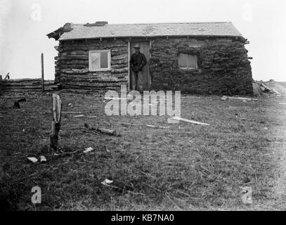 AJAXNETPHOTO. 1903. KANADA, GENAUER ORT UNBEKANNT. - ANMERKUNG AUF GLASPLATTE 'HAL. SHACK“. MANN IN NORDWEST-POLIZEIUNIFORM, DIE VOR EINER BLOCKHÜTTE POSIERT, MIT TORF, DER DIE HALBE FASSADE BEDECKT. FOTOGRAF:UNBEKANNT © DIGITAL IMAGE COPYRIGHT AJAX VINTAGE PICTURE LIBRARY QUELLE: AJAX VINTAGE PICTURE LIBRARY COLLECTION REF:AVL 2373 Stockfoto