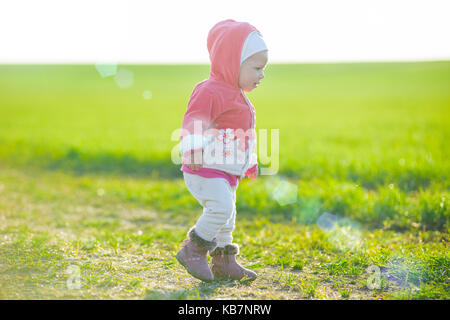Glückliche kleine Mädchen zu Fuß auf der Wiese und Blick auf Sonne Stockfoto