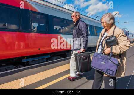 Ein älteres Ehepaar stand auf einer Plattform, über die an Bord eine Jungfrau Zug nach Kings Cross Bahnhof in Peterborough, Cambridgeshire, England, UK. Stockfoto