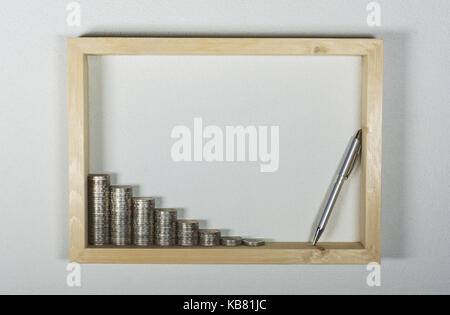 Münze mit Pen in Holzrahmen auf weißer Wand Hintergrund stack. Finanzielle und speichern. Stockfoto