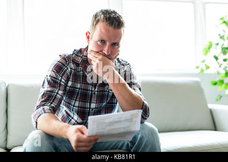 Mann hält einige Dokumente auf Sofa Wohnzimmer Schockiert Stockfoto