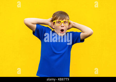 Portrait von sommersprossigen Jungen mit entsetzten Gesicht. Hände halten in der Nähe von Kopf, Mund und Kamera. Studio shot, gelber Hintergrund Stockfoto