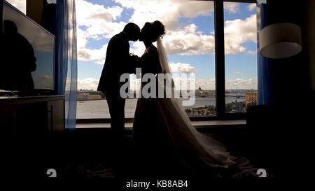 Die Braut und der Bräutigam stand vor dem Fenster und küssen sich. Braut und Bräutigam, der vor dem Fenster und zusammen irgendwo suchen. Schatten Stockfoto