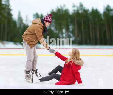 Mann Frau zu helfen, sich auf der Eislaufbahn Stockfoto