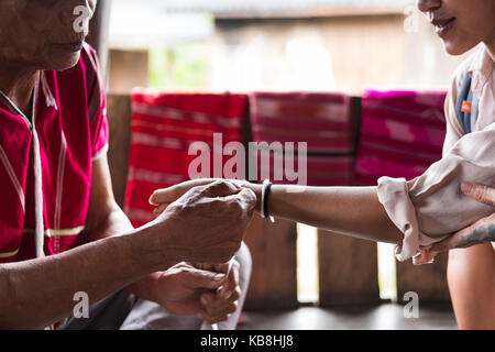 Chiang Mai, Thailand - 14. September 2017: unbekannte ältere Mann von Karen Hill Tribe der ethnischen Minderheit Riegel gast Handgelenk für Segen in binden Ceremo Stockfoto
