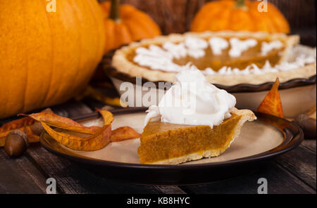 Eine Scheibe einer Pumpkin Pie mit Schlagsahne serviert. Kürbisse und Herbst Dekorationen auf rustikalen Tabelle angezeigt. Stockfoto