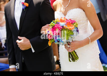 Eine Orange, Rosa, Rot, Gelb, Blau Bouquet von einer Braut gehalten wird, gehen hinunter den Gang mit ihrem Vater. Stockfoto