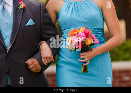 Eine Orange, Rosa, Rot, Gelb Bouquet von eine Brautjungfer trägt ein blaues Kleid, gehen hinunter den Gang mit einem trauzeuge. Stockfoto