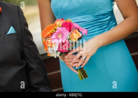 Eine Orange, Rosa, Rot, Gelb Bouquet von eine Brautjungfer trägt ein blaues Kleid, gehen hinunter den Gang mit einem trauzeuge. Stockfoto