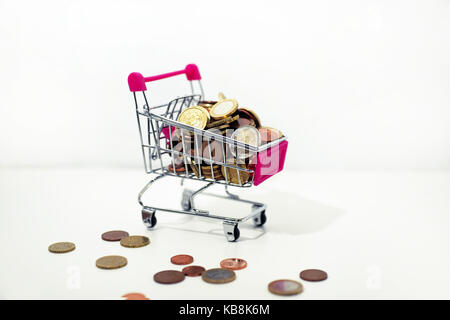 Abstrakte Komposition von etwas zu kaufen. Kleine Wagen mit Münzen auf weißem Hintergrund. Stockfoto