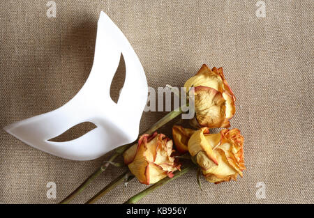 Weiß venezianische Maske und drei trockenen Rosen auf Leinwand Hintergrund Stockfoto