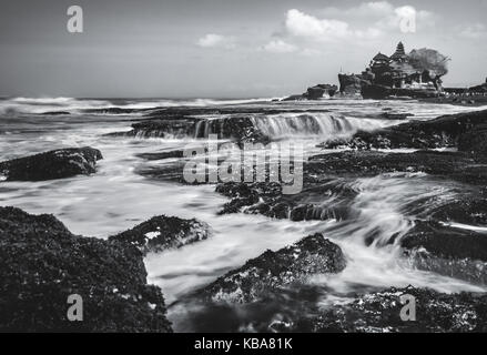 Schwarz-weiß Bild von Tanah Lot in Bali. Atemberaubende natürliche geologische Felsformation mit Uluwatu Tempel historisches Gebäude von der küstennahen Felsen gesehen Stockfoto