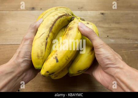 Ein Mann hält ein Bündel Bananen auf Holz- Hintergrund, flach Stockfoto