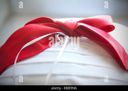 Ein glitzerndes Silber und Diamanten Hochzeit Ring auf einem Ring bearer Kissen mit Red Ribbon Stockfoto