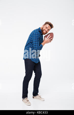 In voller Länge Porträt einer glücklich aussehenden bärtigen Mann, Rugby Ball, und wenn man die Kamera auf weißem Hintergrund Stockfoto
