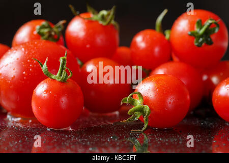 Extreme Nahaufnahme von Frische, Bio Kirschtomaten auf einem schwarzen reflektierenden Hintergrund mit Wassertropfen. selektive Fokus und flache Tiefenschärfe Stockfoto