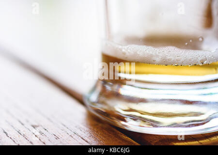 Nahaufnahme der teilweise bearbeiteten kalten Glas Bier mit cremiger Schaum und Blasen auf grober Holztisch Stockfoto