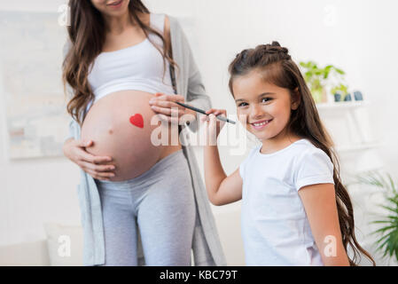 Mädchen Zeichnung auf schwangeren Bauch von Mutter Stockfoto