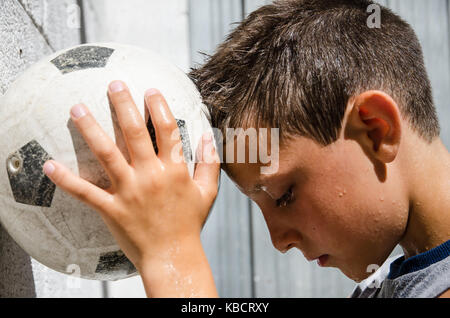 Eine junge verschwitzte Fußballer lehnt sich seine Stirn auf den Ball. Stockfoto