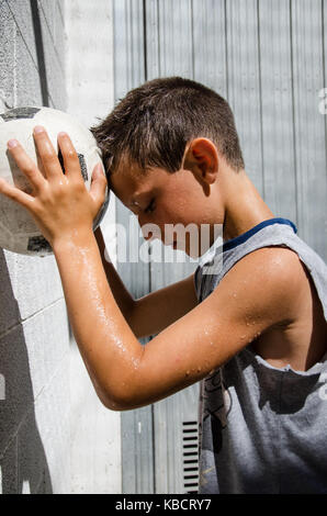 Eine junge verschwitzte Fußballer lehnt sich seine Stirn an die Kugel. vertikale Seite Stockfoto