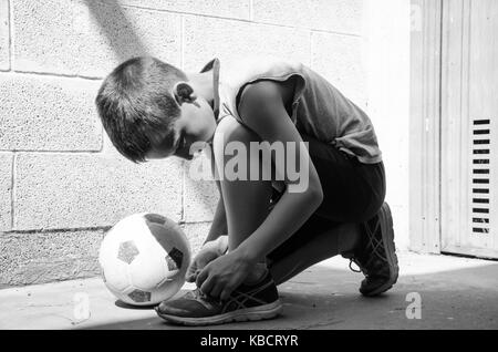 Straße Fußball. Ein junger Fußballer trägt seine Schuhe und ist bereit für ein einsames Training in der Garage. Schwarz-weiß-Bild. Stockfoto