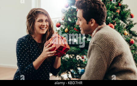 Glückliche junge Frau mit Geschenk Box neben einem Weihnachtsbaum zu Hause sitzen. Paar gute Zeit feiern Weihnachten. Stockfoto