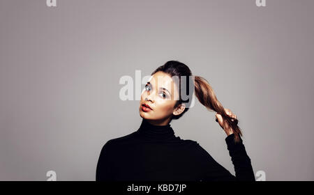 Starkes gesundes Haar. Schöne junge Frau ihren Pferdeschwanz Holding über grauen Hintergrund. Stockfoto