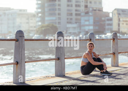 Läuferin, die Pause nach dem Fitness Training im Freien durch das Meer. Frau entspannend nach Morgen laufen auf der Straße durch das Meer. Stockfoto