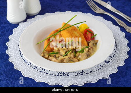 Kartoffel Bratlinge mit Pilzrahmsauce in eine weiße Platte auf einem blauen Tuch. Gesunde Ernährung Konzept Stockfoto