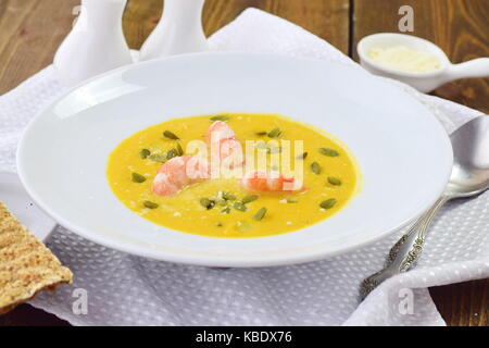 Kürbispüree Suppe mit Garnelen in eine weiße Platte auf einem hölzernen Hintergrund. Gesunde Ernährung Konzept Stockfoto