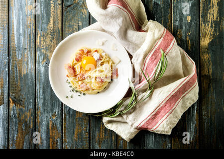 Traditionellen italienischen Pasta alla Carbonara mit Eigelb, bauchspeck Speck, Parmesan, Thymian, in weißen Teller serviert auf Textilien Bettwäsche über alte Holz- Pla Stockfoto