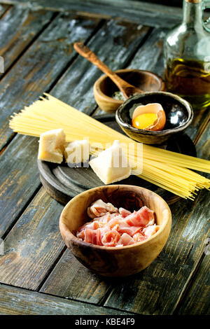 Zutaten für traditionelle italienische Pasta alla Carbonara. Ungekochte Spaghetti, bauchspeck Speck, Parmesan, Eigelb, Salz, Pfeffer in Olivenholz bo Stockfoto