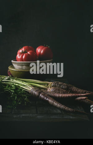 Schüssel Tomaten mit violetten Karotte, Zwiebel auf alten hölzernen Küchentisch. Dunklen rustikalen Still Life. Stockfoto