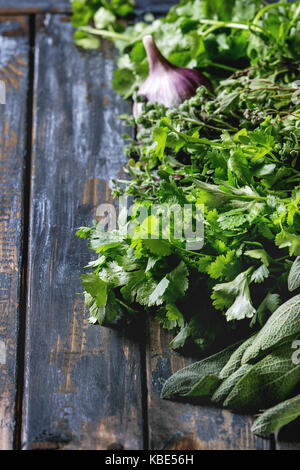 Auswahl an frischen Kräutern Koriander, Salbei, Oregano, Knoblauch über alte Holzbrett Hintergrund. Nahaufnahme mit dem Raum. Stockfoto