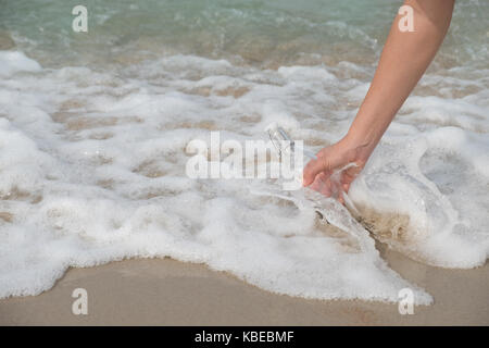 Hand hält eine Flasche mit einem Brief, der nach innen durch das Meer eingefügt. Stockfoto