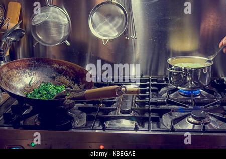 Gasoven mit Wok und Spinat und kleine Pfanne auf Feuer Stockfoto