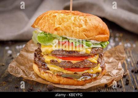 Große Hamburger mit drei Rind Schnitzel und Gemüse auf Holz Hintergrund. Makro. Stockfoto