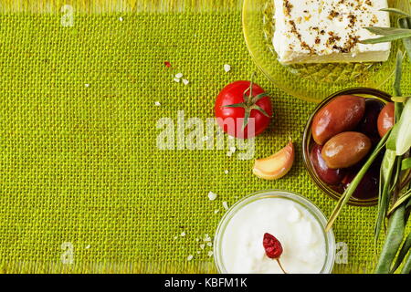 Grüner Hintergrund Tuch mit den Platz für einen Text. Traditionelle mediterrane Motiv - Feta Käse, Tzatziki, Oliven, Knoblauch, Glas mit Olivenöl, Tomaten, Stockfoto