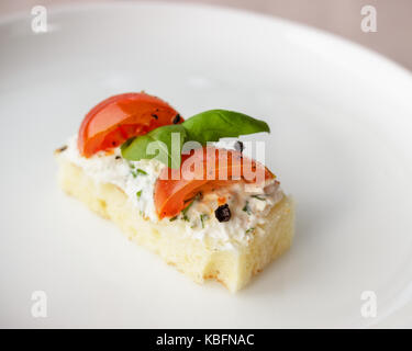 Mit Hüttenkäse, Basilikum und Strauchtomaten auf weiße Platte Canape. Festliche Vorspeise hautnah. Selektiver Fokus Stockfoto