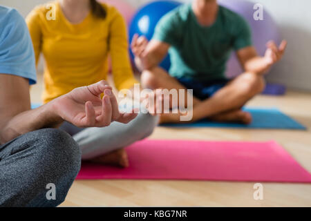 Mittelteil der Yoga Lehrer mit Schülern der Meditation im Lotussitz im Health Club Stockfoto