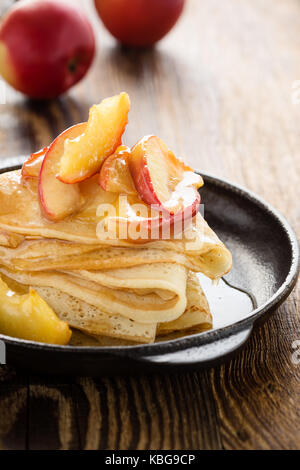 Hausgemachte crepes serviert mit frischem karamellisierten Äpfeln und Karamellsauce in Gusseisen Skillet auf ländlichen Holztisch Stockfoto