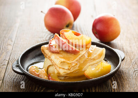 Hausgemachte crepes serviert mit frischem karamellisierten Äpfeln und Karamellsauce in Gusseisen Skillet auf ländlichen Holztisch Stockfoto