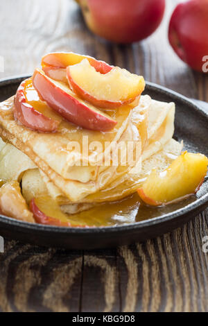 Hausgemachte crepes serviert mit frischem karamellisierten Äpfeln und Karamellsauce in Gusseisen Skillet auf ländlichen Holztisch Stockfoto