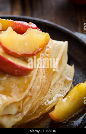 Hausgemachte crepes serviert mit frischem karamellisierten Äpfeln und Karamellsauce in Gusseisen Skillet auf ländlichen Holztisch Stockfoto