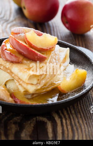 Hausgemachte crepes serviert mit frischem karamellisierten Äpfeln und Karamellsauce in Gusseisen Skillet auf ländlichen Holztisch Stockfoto